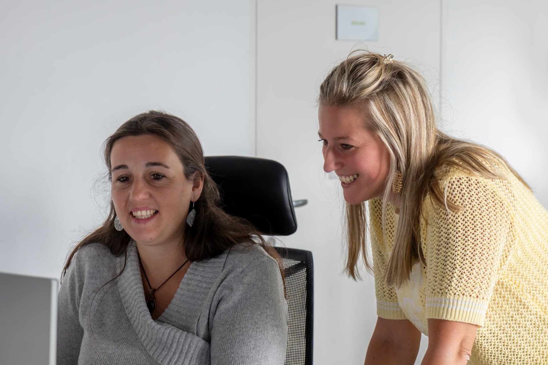 Twee collega's lachen samen achter een computerscherm op de klantendienst